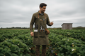 Person in strawberry patch wearing waxed canvas apron with pruning shears, gloves, and notepad